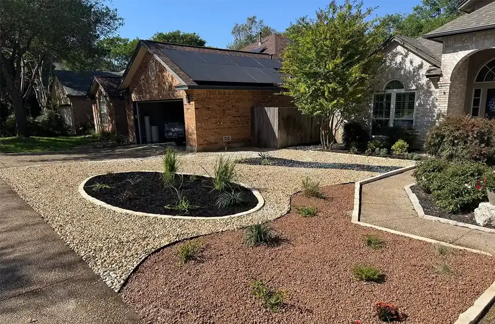 A modern front yard features drought-resistant landscaping with gravel, rocks, and sparse plants. A circular bed with ornamental grasses sits near a driveway, and a house with solar panels is in the background.